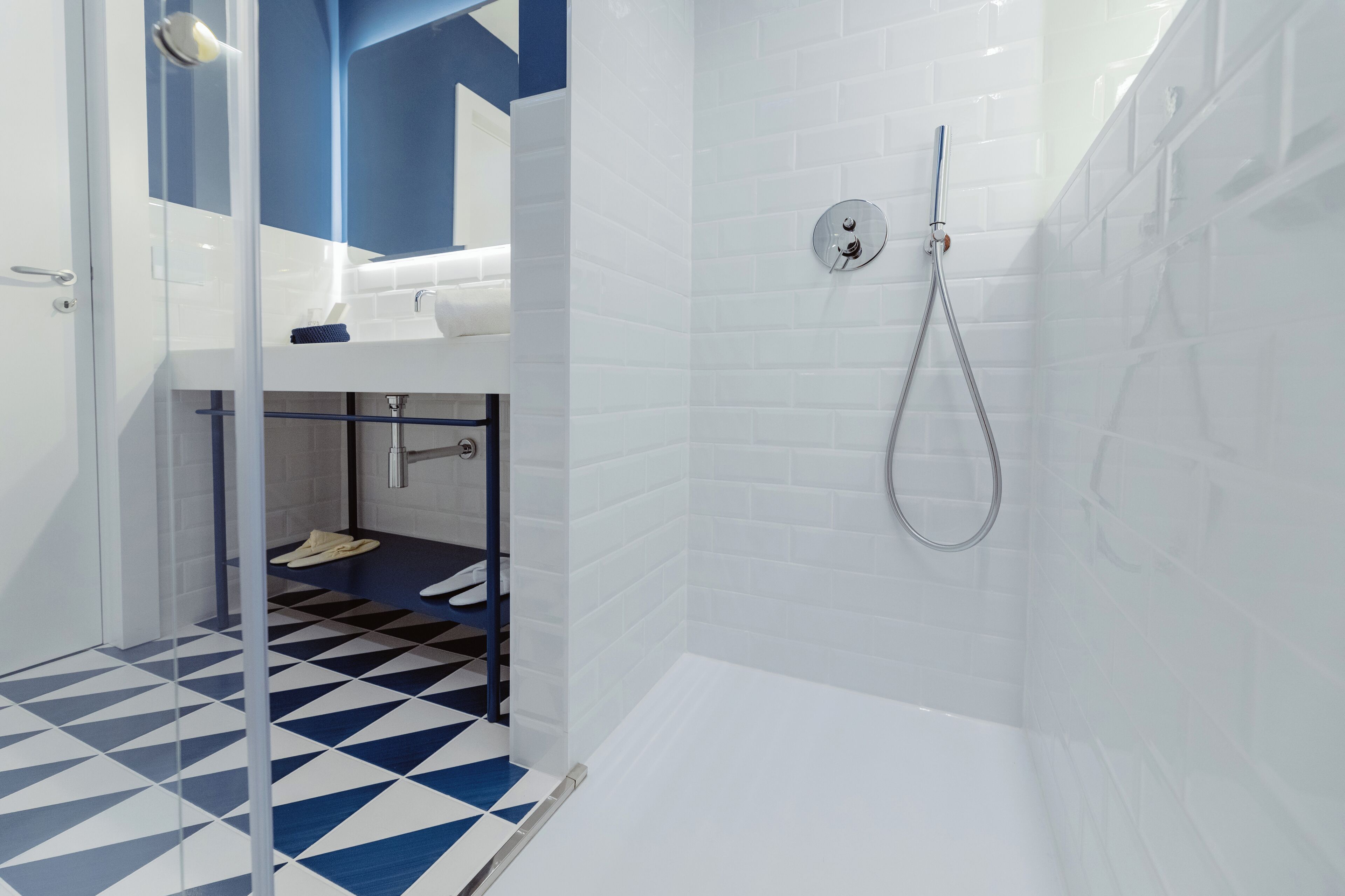 A modern bathroom with a geometric patterned floor, a shower with a handheld hose, and a visible sink area.