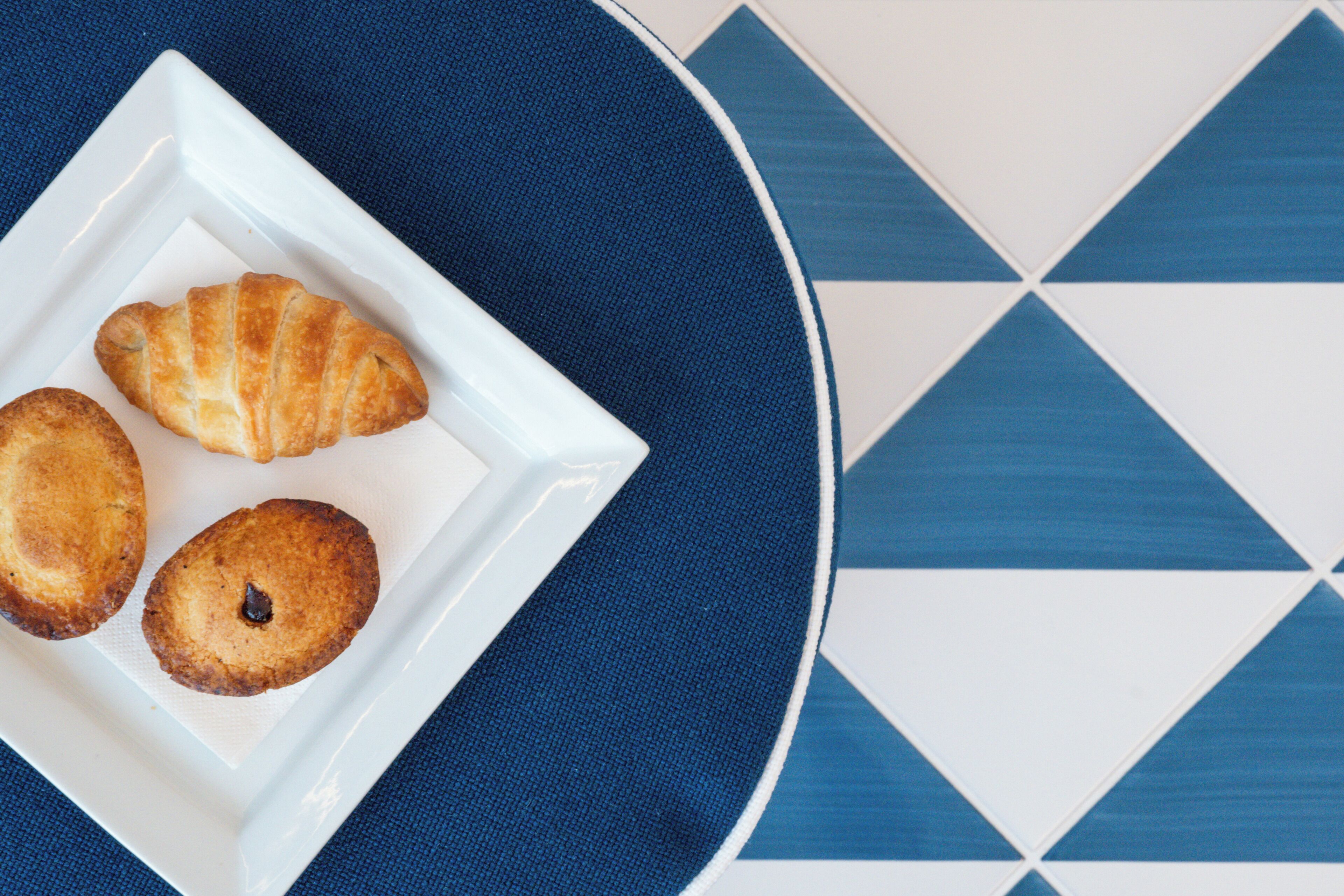 A white plate with three pastries on a blue and white patterned tablecloth.