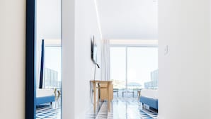 A hotel hallway with a geometric patterned floor, a large mirror, and a staircase leading to a balcony with a bed.