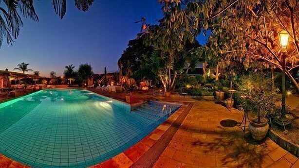 A swimming pool with a tiled deck, surrounded by palm trees and outdoor seating areas. - Gianferrante (Paterno)