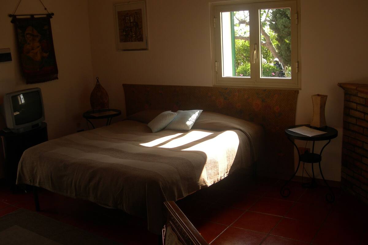 A bedroom with a bed, a television, a window, and a small table.
