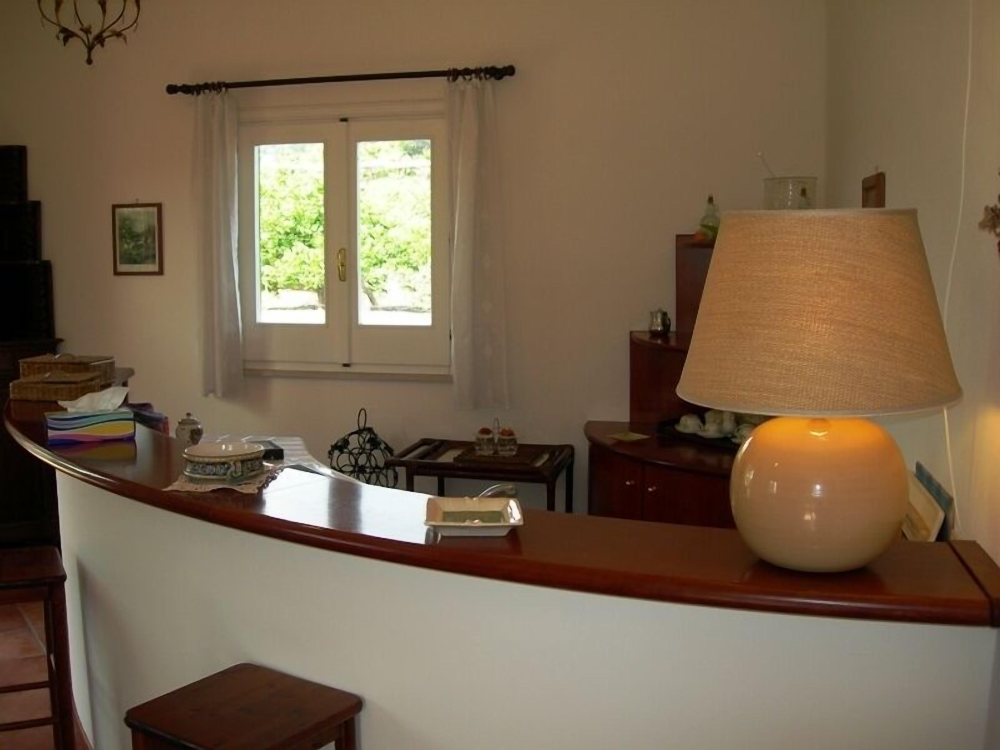A cozy kitchen with a wooden counter, a table, and a lamp. There is a window with curtains, a picture on the wall, and various kitchen items on the counter.