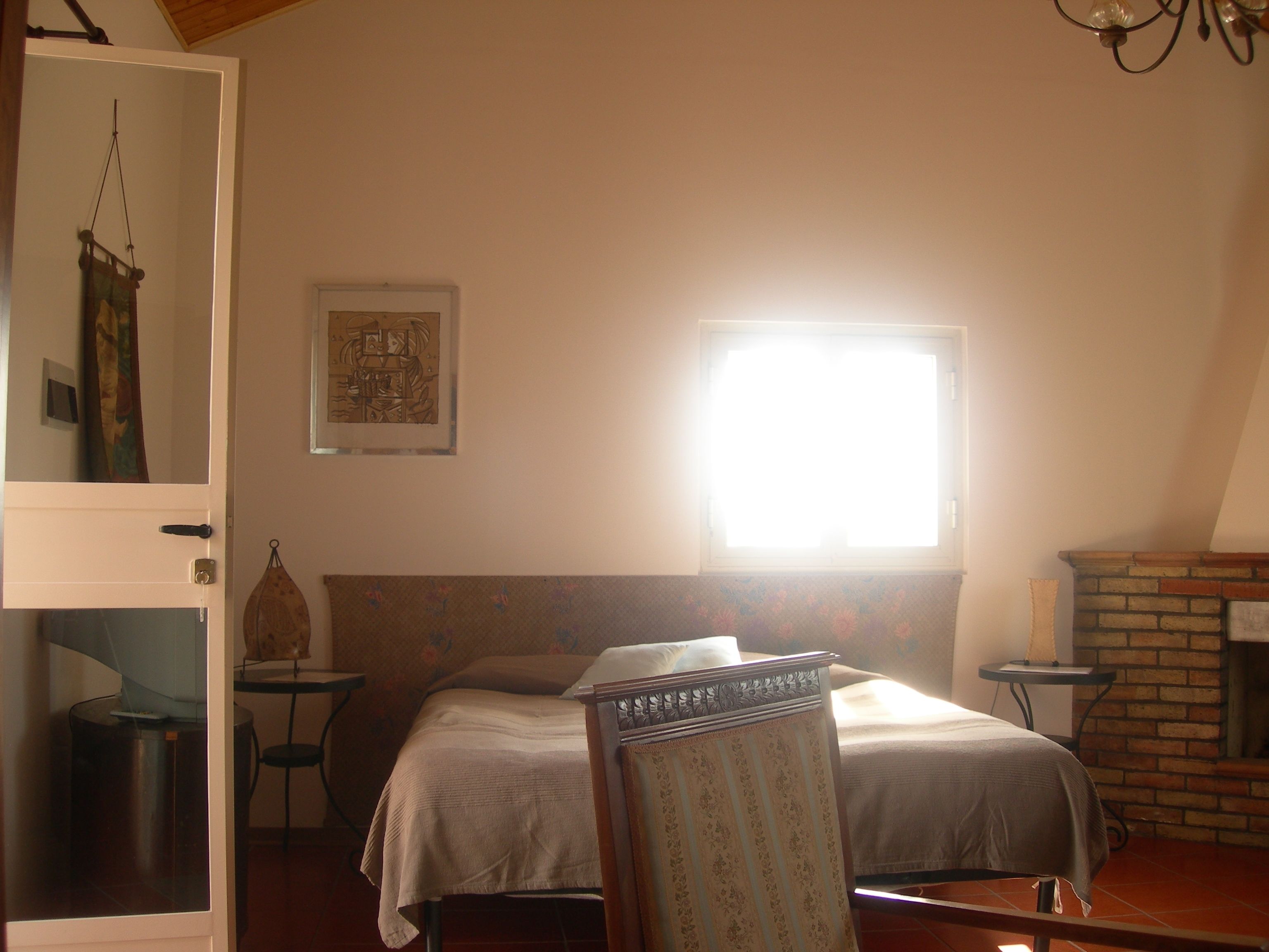 A bedroom with a bed, a chair, a small table, a fireplace, and a window.
