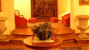 A lobby with a large painting, red armchairs, and a central table with a floral arrangement. - Gianferrante (Paterno)