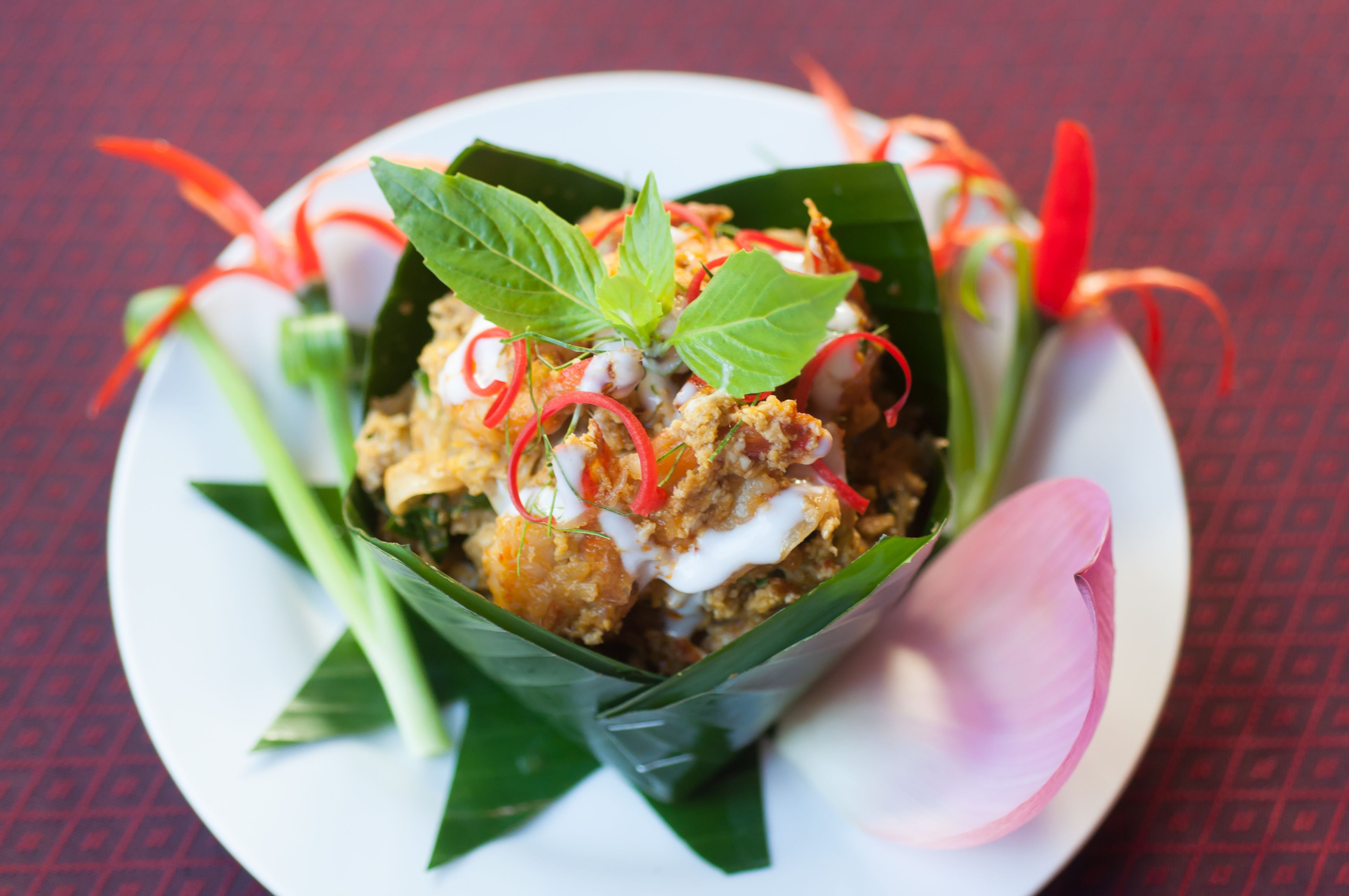 A dish in a leaf bowl with green leaves, red chili, and white sauce.