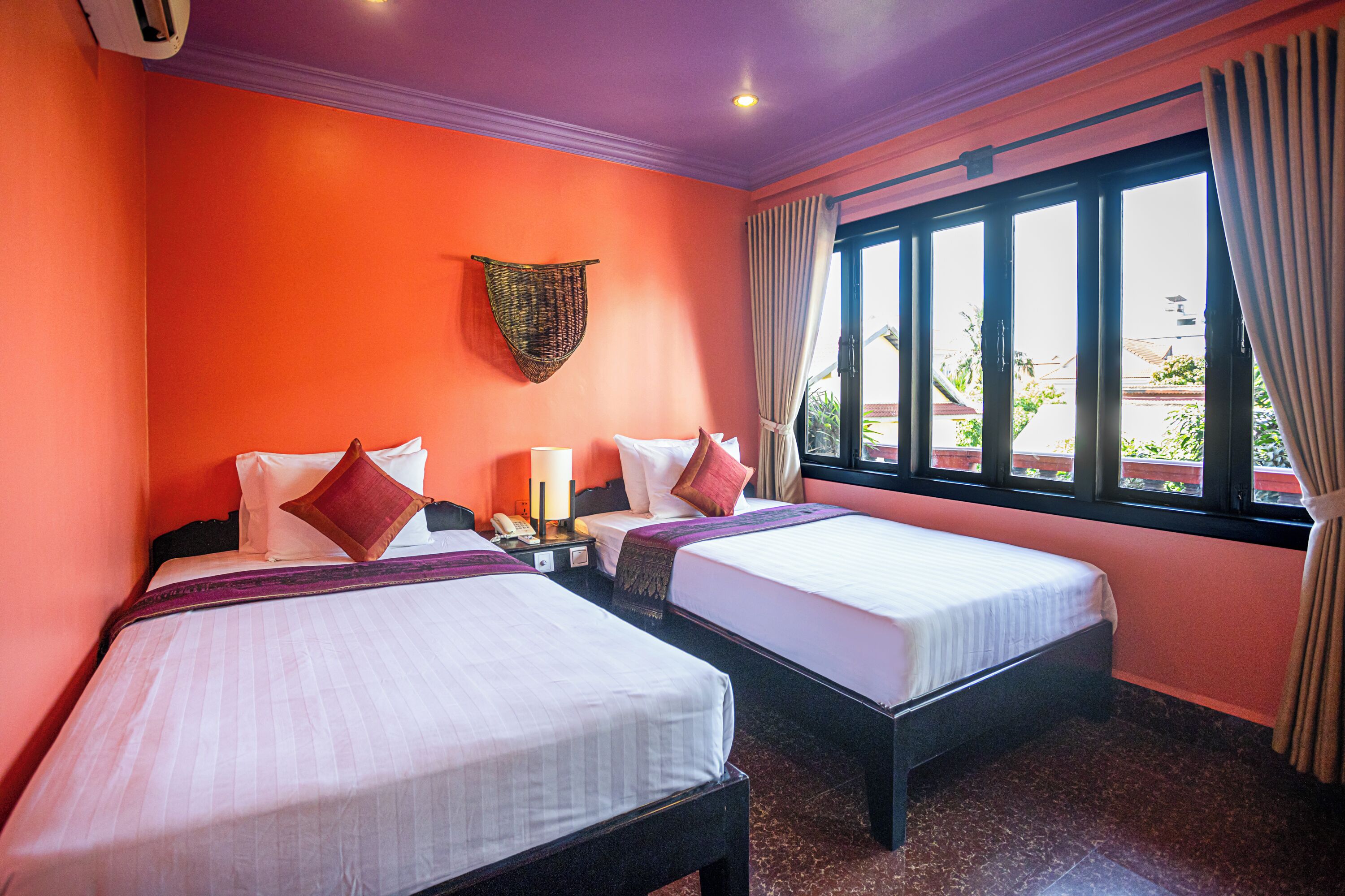 A hotel room with two beds, a window with curtains, a wall-mounted telephone, and a ceiling light.