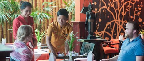 Un restaurante con mesas dispuestas para comer, un camarero atendiendo a los comensales y una estatua decorativa de Buda.