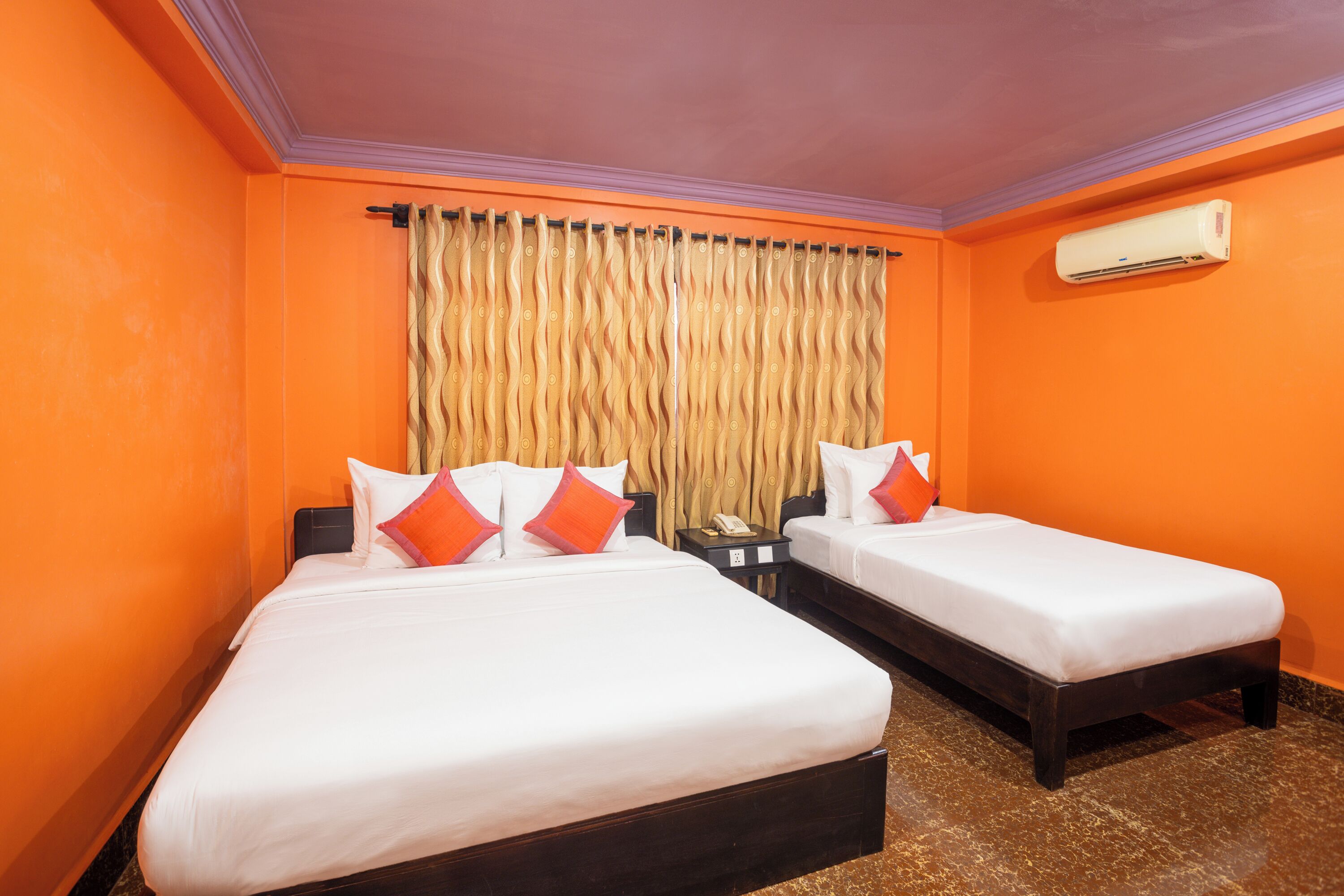 A hotel room with two beds, an air conditioning unit, a curtain, and a telephone on a nightstand.