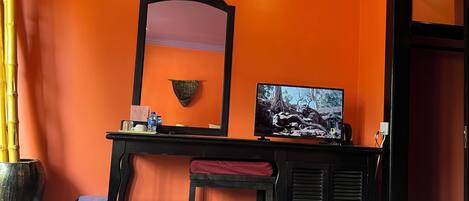 Ett hotellrum med orange väggar, en stor spegel, en platt-TV, ett skrivbord med en röd stol och två sängar.