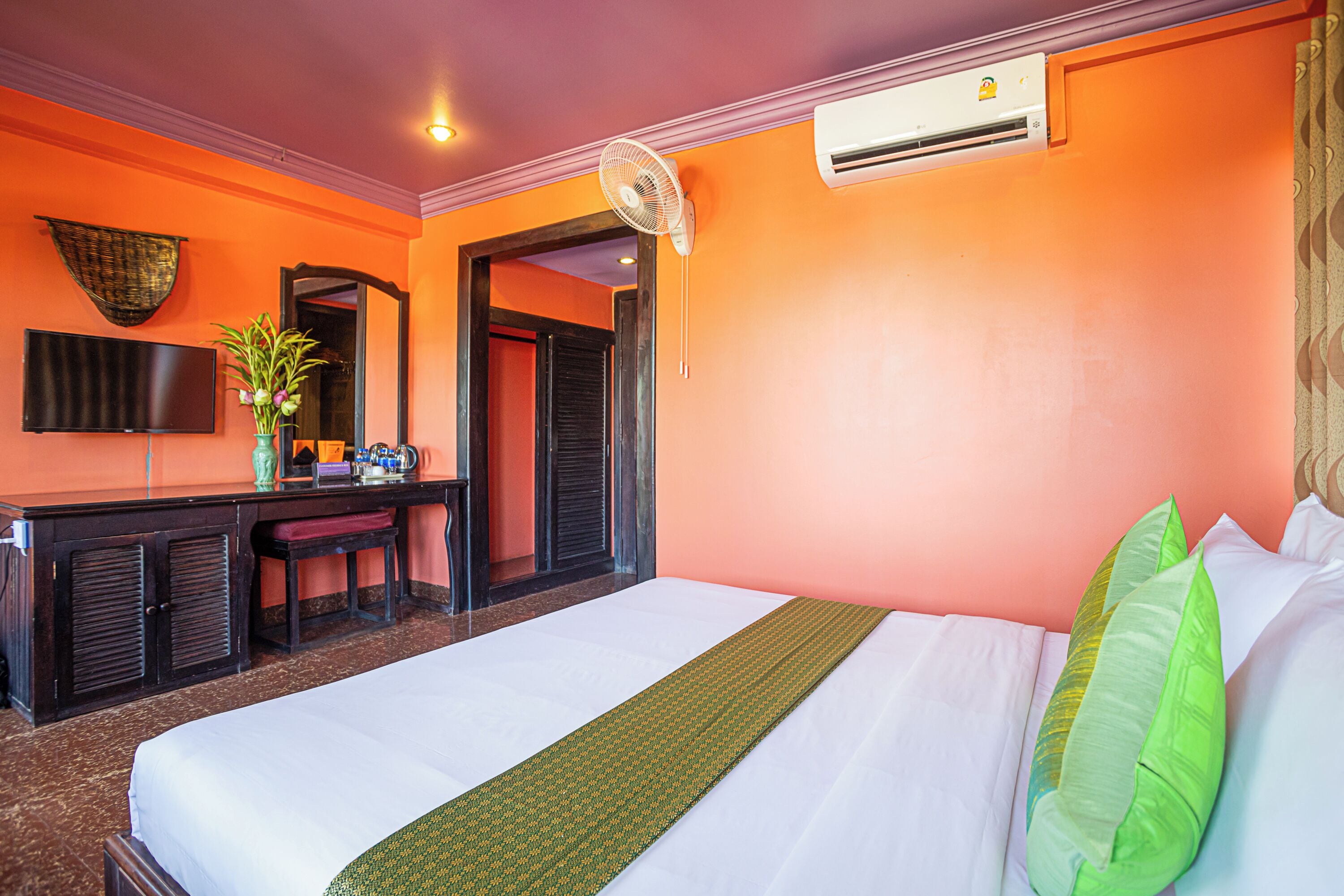 Quarto de hotel com cama, escrivaninha, cadeira, televisão e aparelho de ar condicionado.