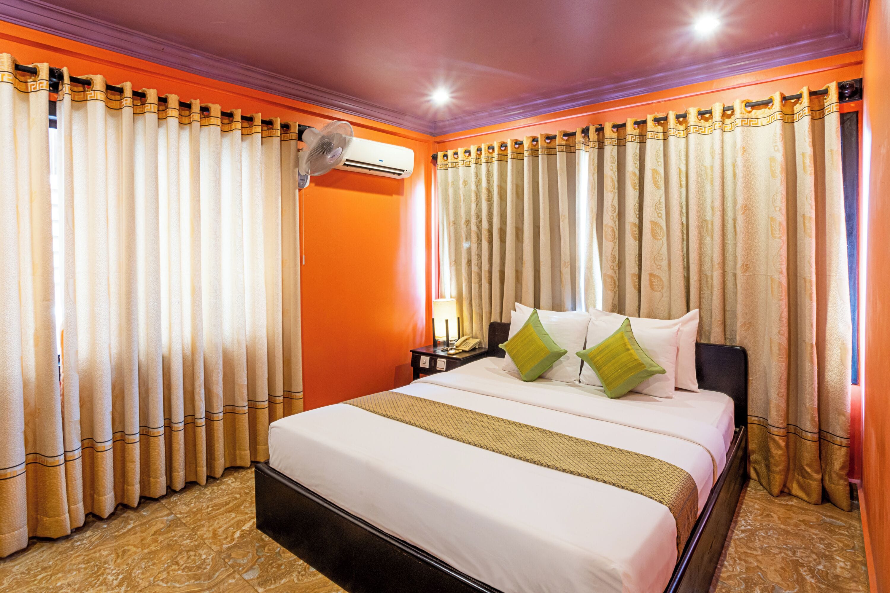 Una camera d'albergo con un letto, tende, un condizionatore, un comodino e una lampada.