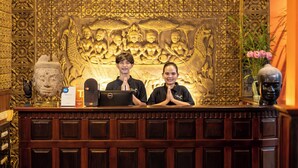 A reception desk with intricate carvings, a statue, and a vase with flowers. - Golden Butterfly Villa (Siem Reap)