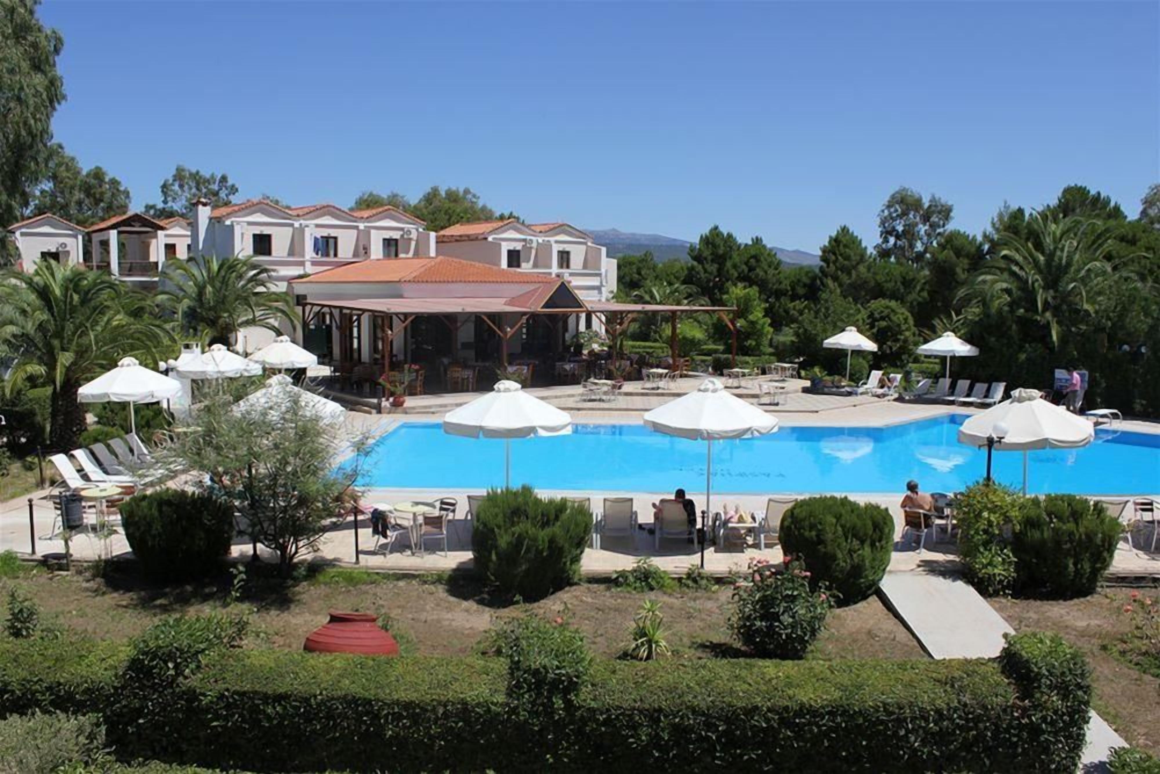A pool area with lounge chairs and umbrellas, surrounded by buildings and greenery.