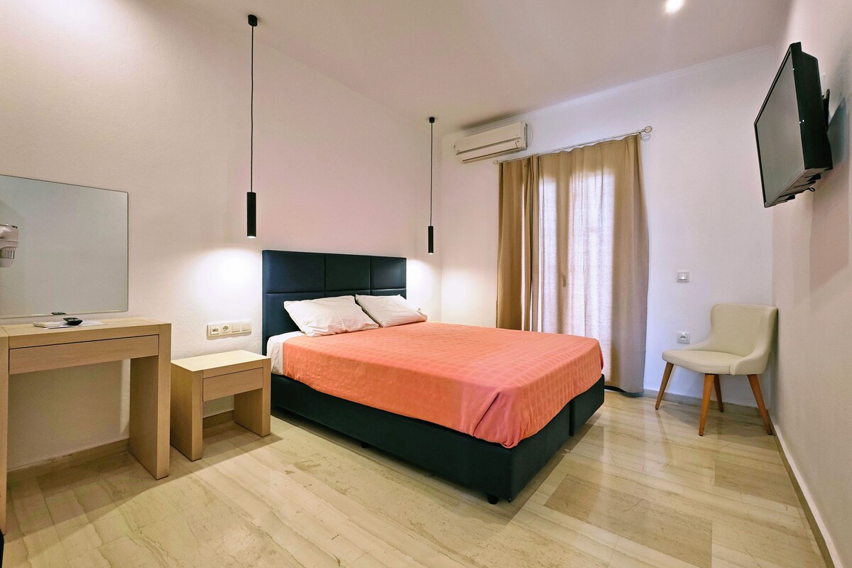A bedroom with a bed, a desk, a chair, a TV, and an air conditioning unit.