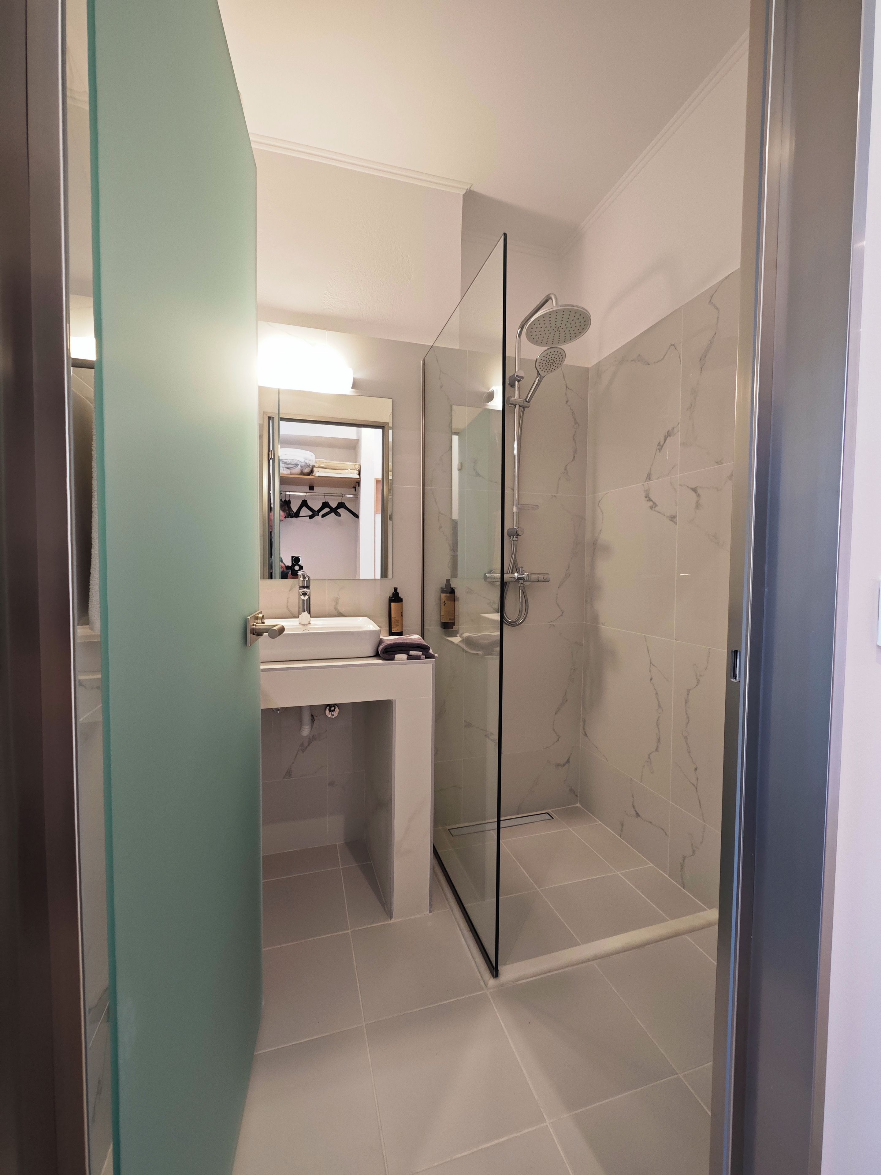 A modern bathroom with a glass shower enclosure, a sink with a mirror above, and a towel rack.