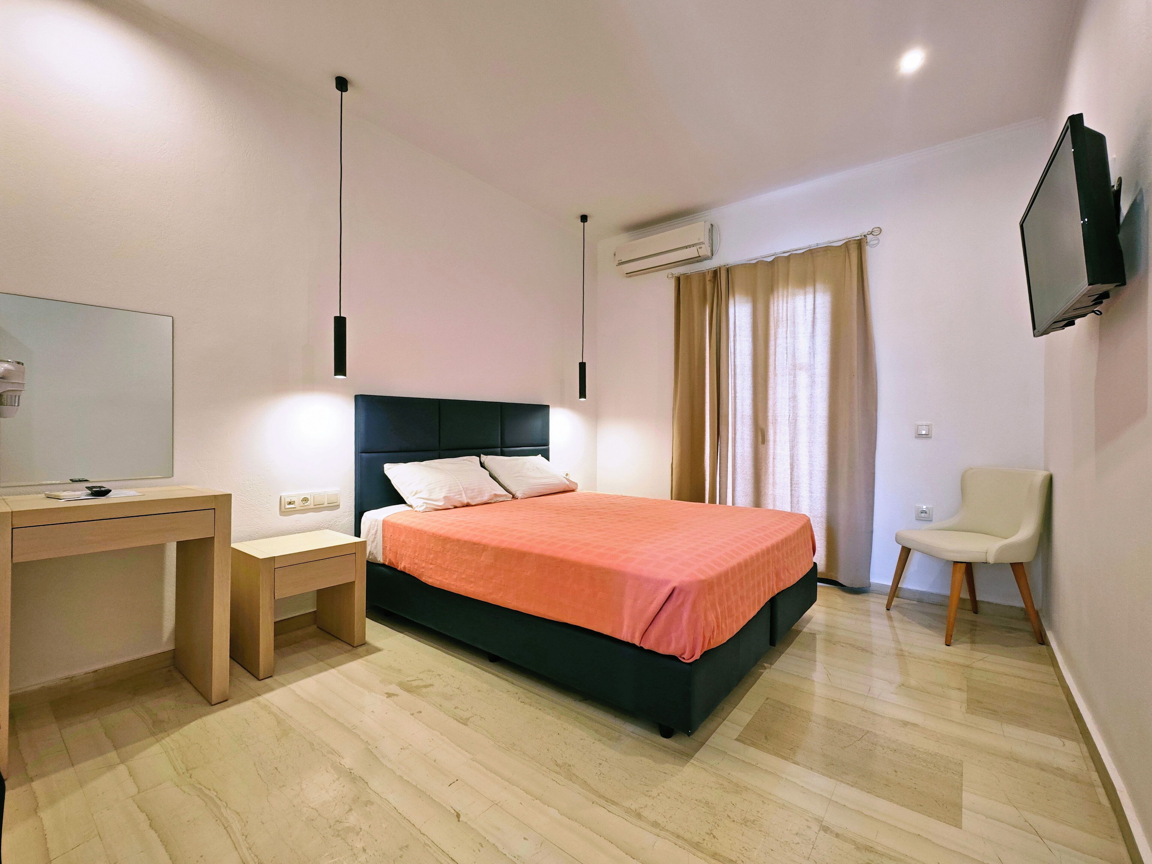 A bedroom with a bed, a desk, a chair, a TV, and an air conditioning unit.