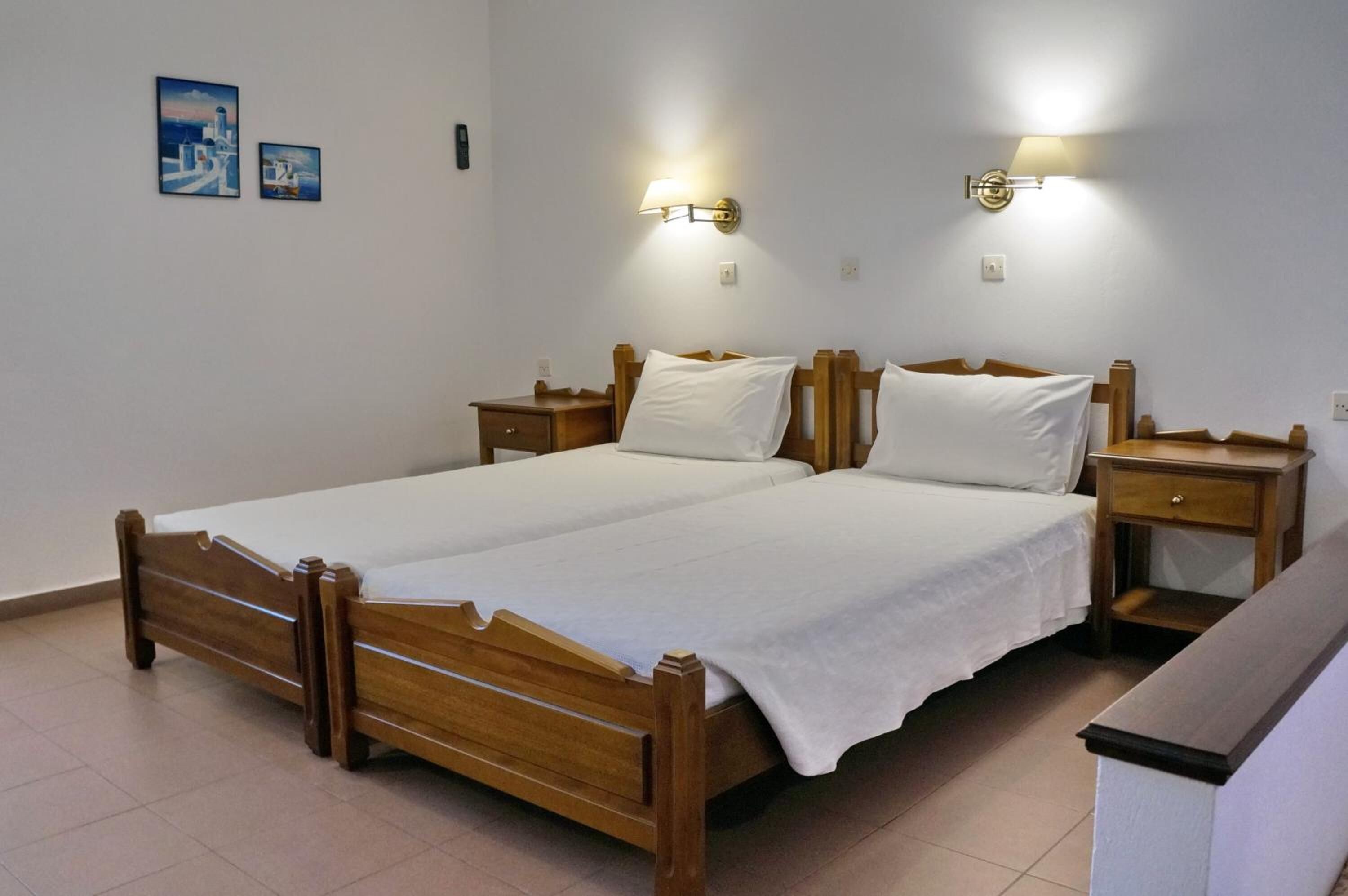Een tweepersoonsbed met houten hoofdborden en nachtkastjes, twee wandlampen en twee ingelijste foto's aan de muur.