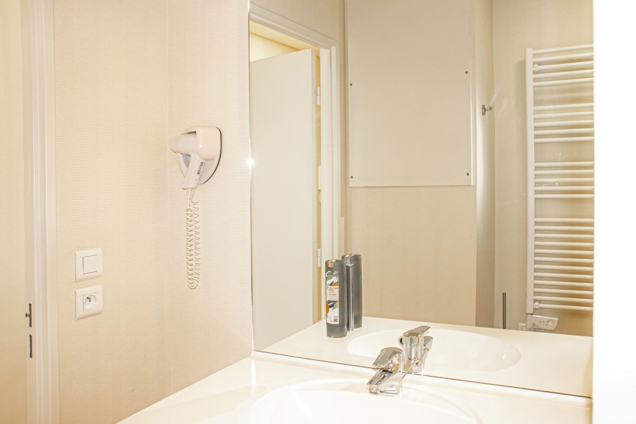 A bathroom with a white sink, a mirror, a hairdryer, and a towel rack.