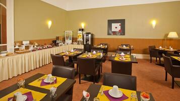 A dining area with tables set for meals, a buffet line, and wall-mounted light fixtures.
