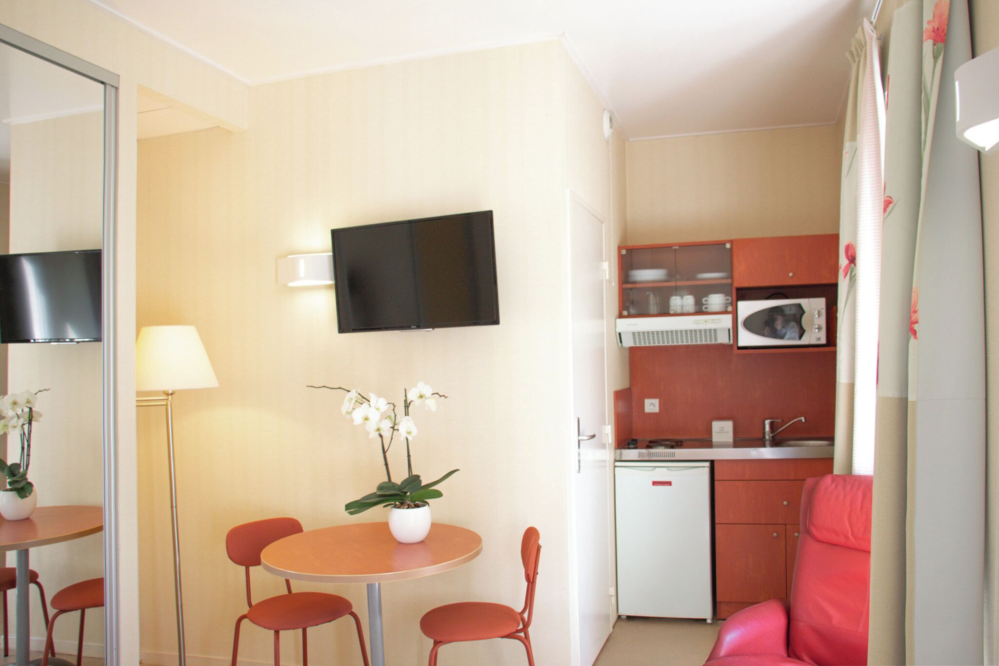 A compact hotel room with a dining area, a small kitchenette, a flat-screen TV, a single bed, and a bathroom.
