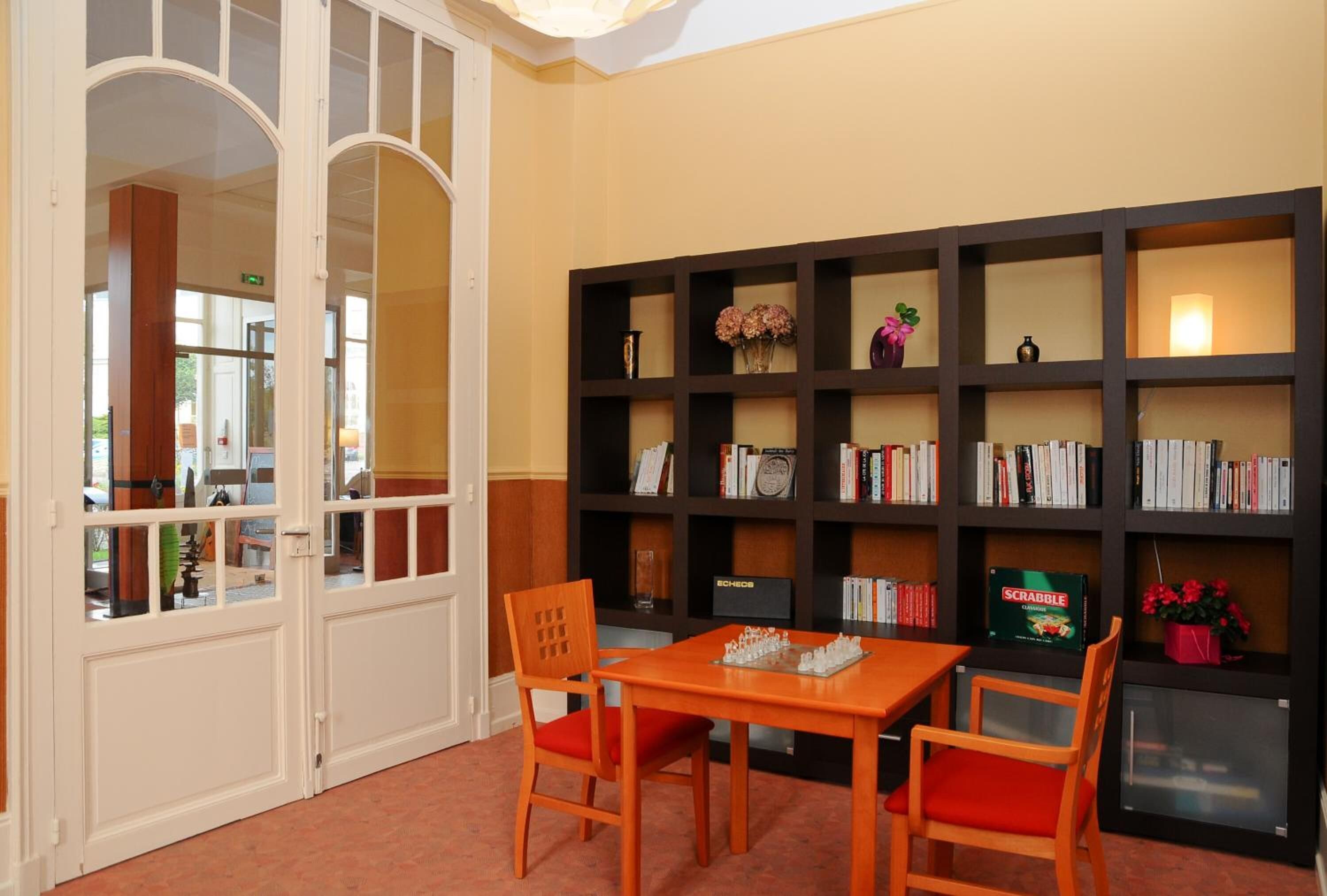 A room with a wooden table and chairs, a bookshelf with books and decorative items, and a door with glass panels.