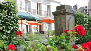 Een gebouw met een witte gevel, rode bloemen in potten en een balkon met een groene parasol.