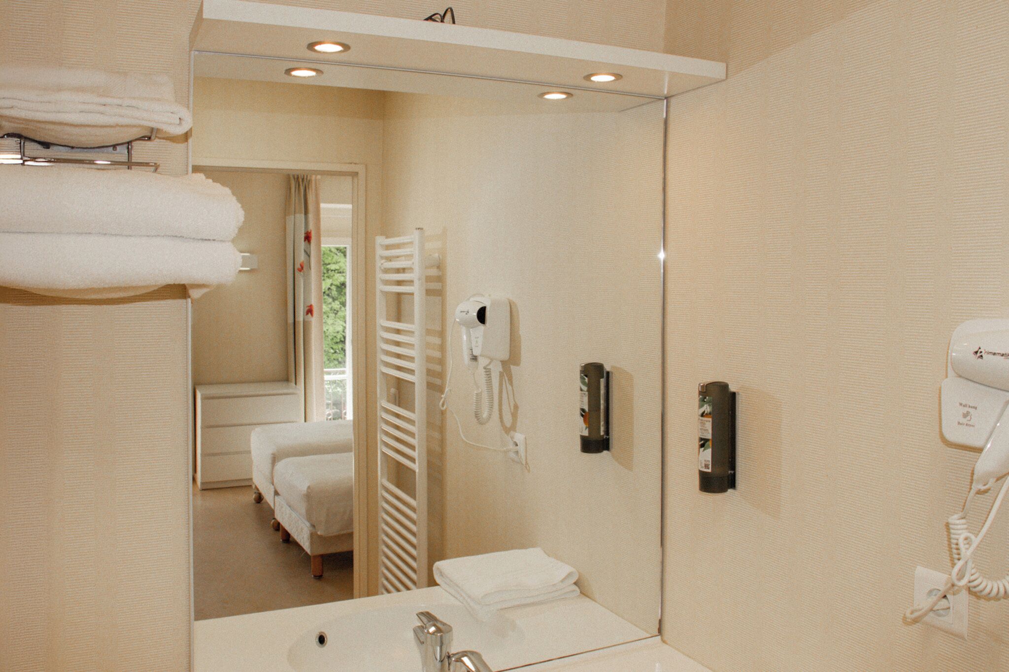 Un baño de hotel con lavamanos, perchero para toallas y dos secadores de pelo.
