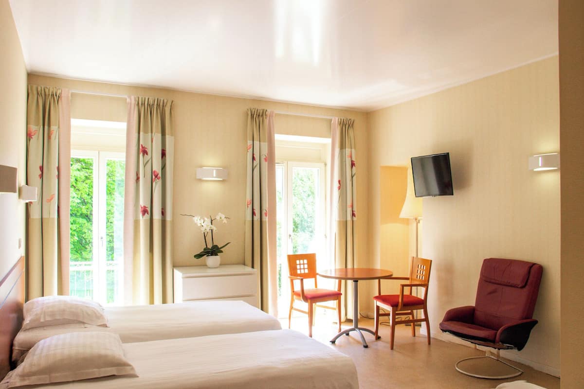 Habitación de hotel con dos camas, televisión, escritorio con sillas y ventana con cortinas.