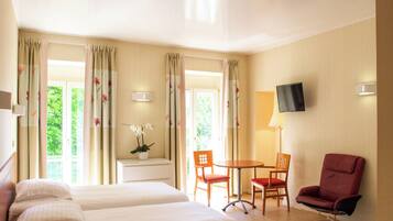 Quarto de hotel com duas camas, televisão, escrivaninha com cadeiras e janela com cortinas.