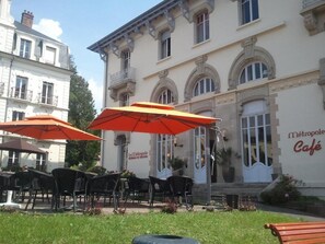 Un café al aire libre con mesas y sillas bajo sombrillas rojas, frente a un edificio con un letrero que dice "Le Métropole Café".