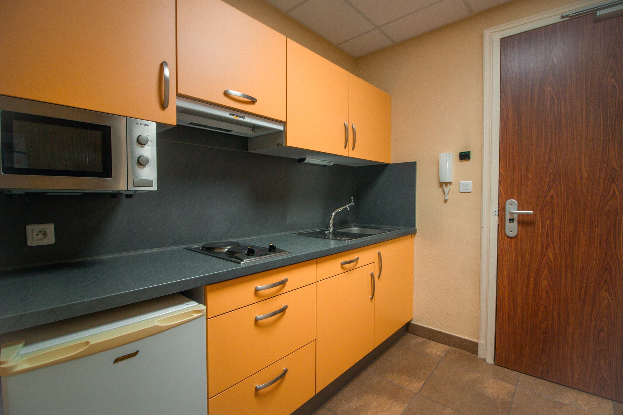 A kitchen with a microwave, stove, sink, and orange cabinets.