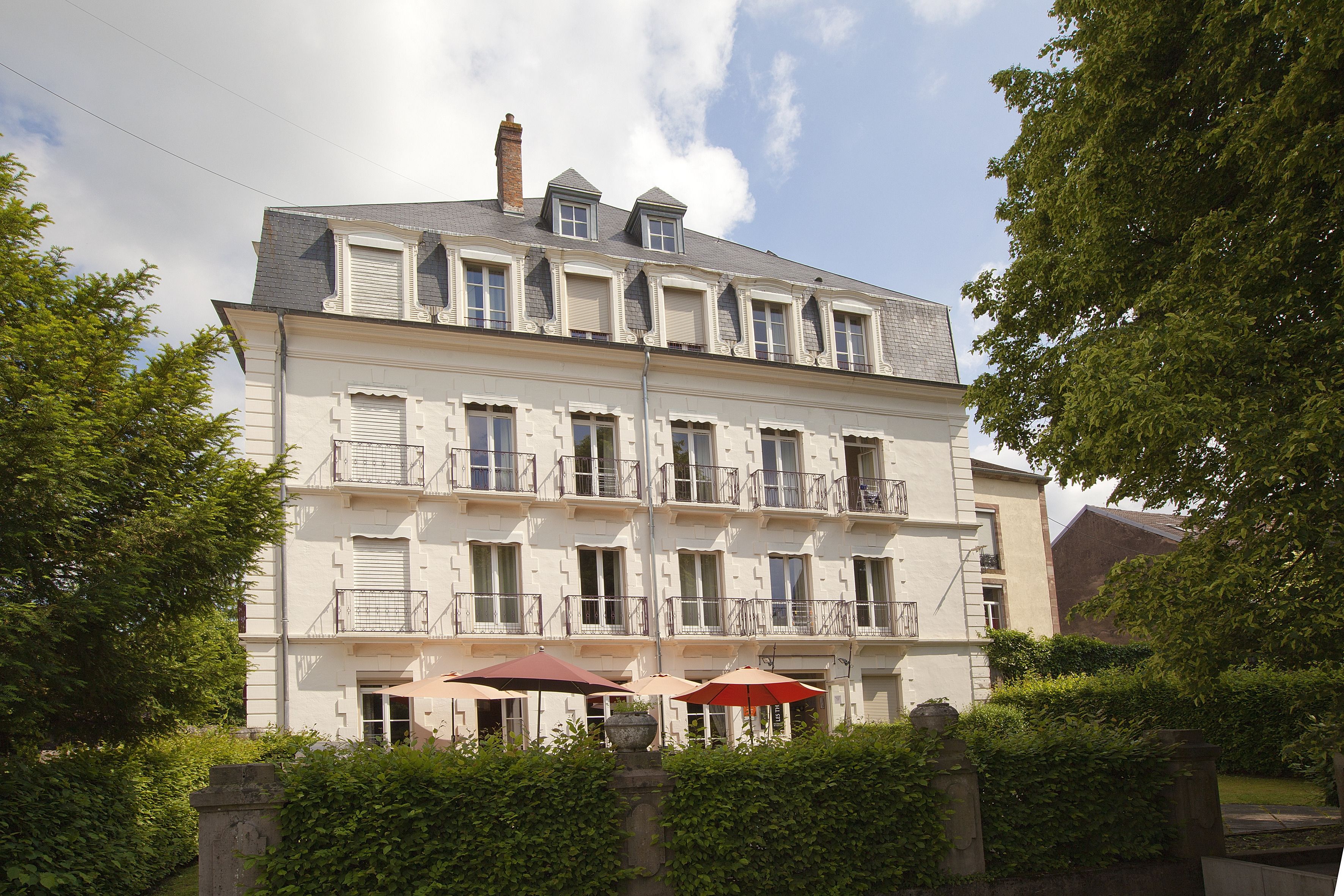 Un immeuble à plusieurs étages doté de balcons et d’un espace jardin agrémenté de parasols.