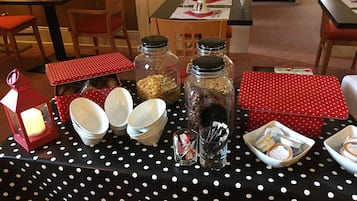 Een eethoek met een zwarte tafelkleed met witte stippen, rode tafelrunners met stippen, en verschillende servies en containers.