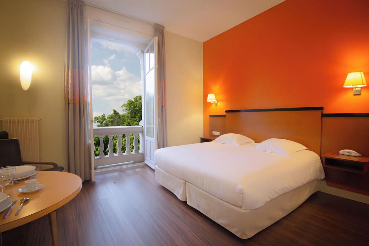 Habitación de hotel con una cama grande, una mesa de comedor con platos y cubiertos, un teléfono y vistas a zonas verdes por la ventana.