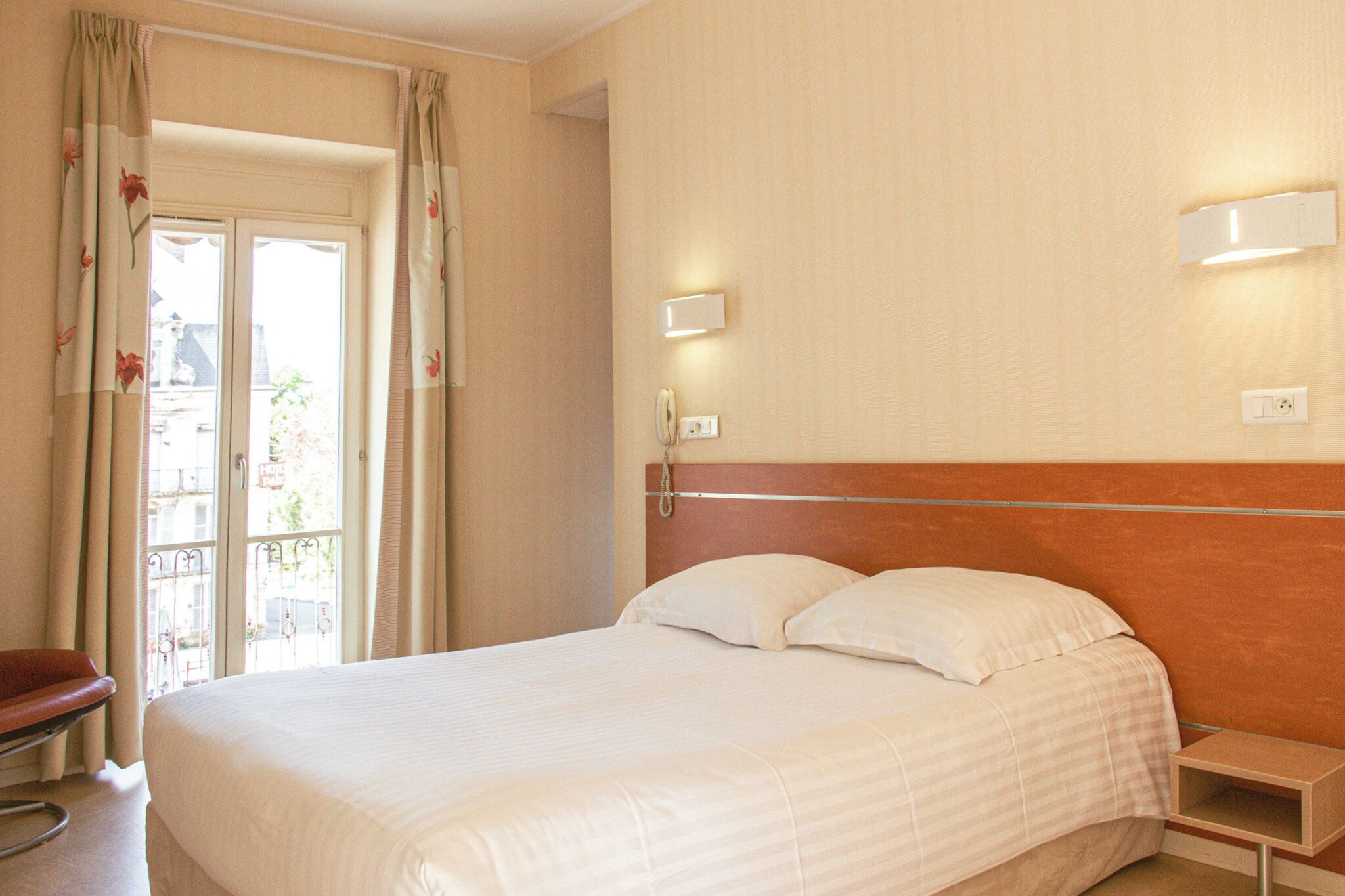 A hotel room with a bed, bedside table, and a window with curtains.