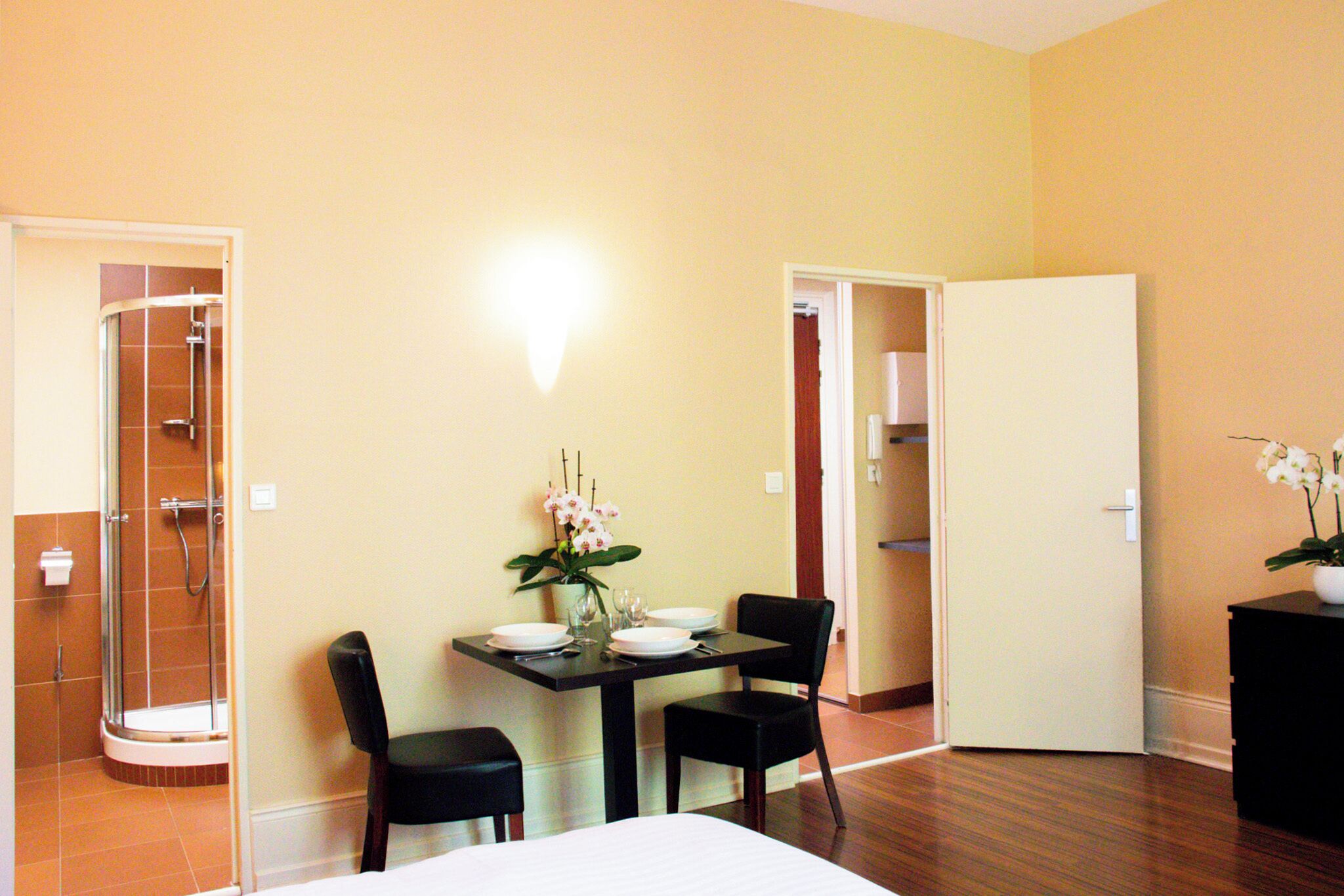 A hotel room with a shower, a dining table with chairs, and a bed.