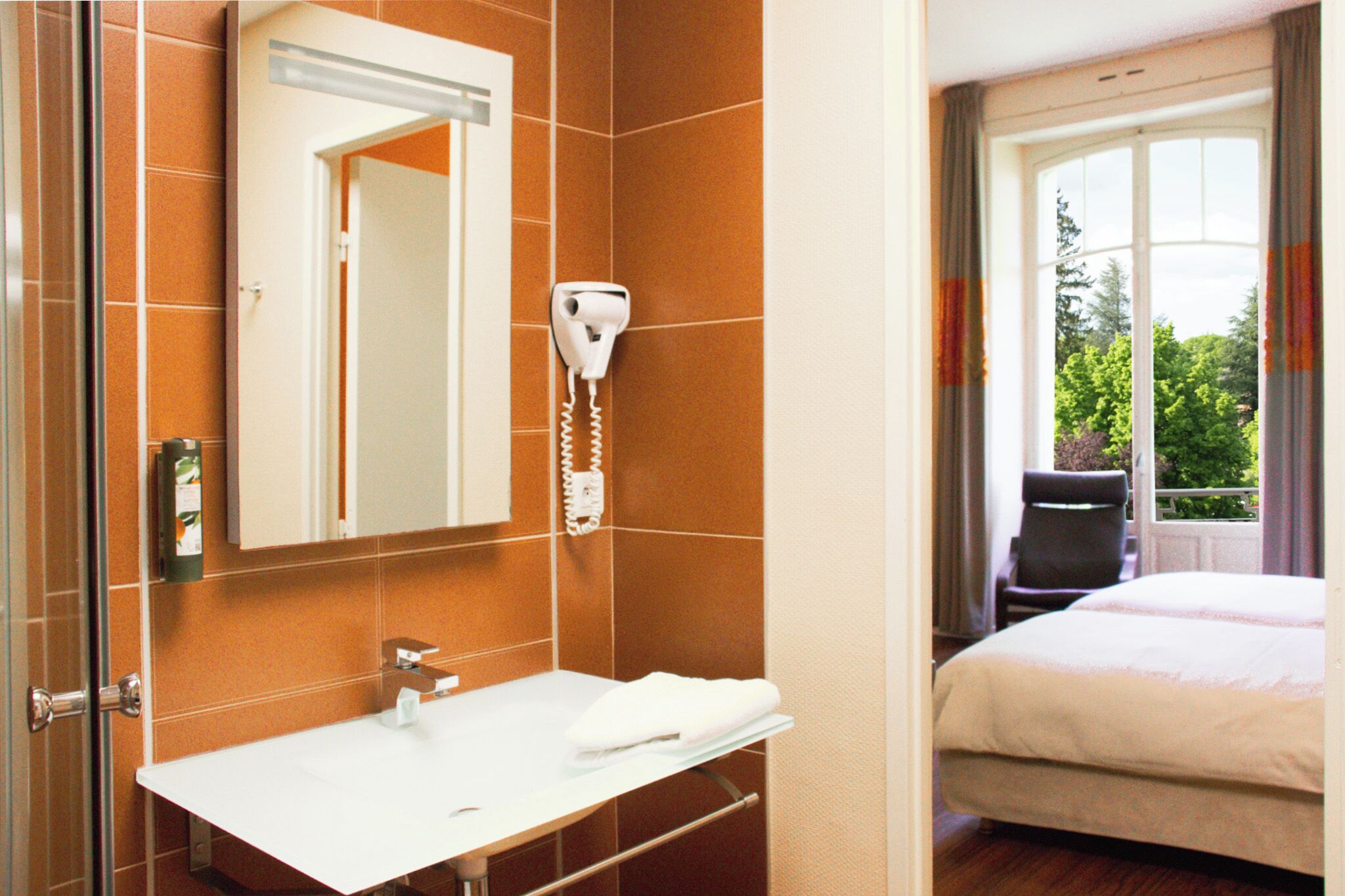 A hotel bathroom with a white sink, a mirror, and a hairdryer mounted on the wall.
