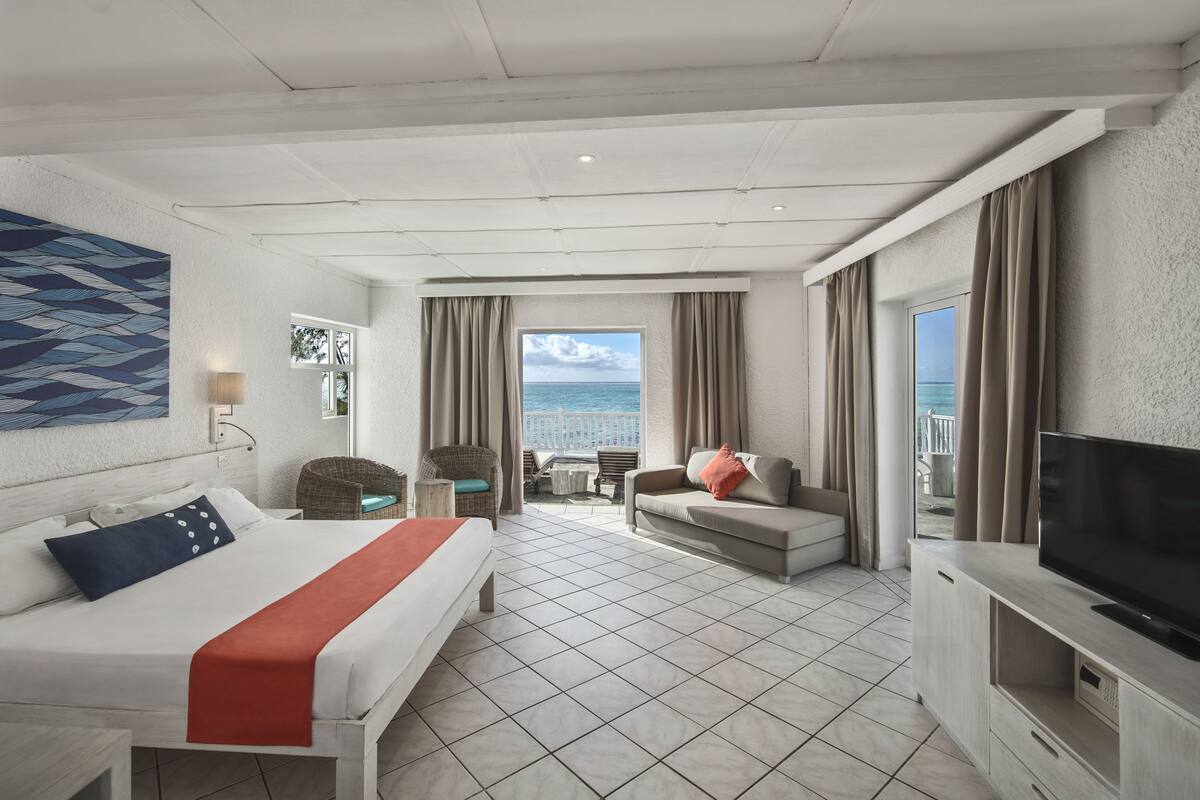 A hotel room with a bed, a sofa, a TV, and a balcony with a view of the sea.