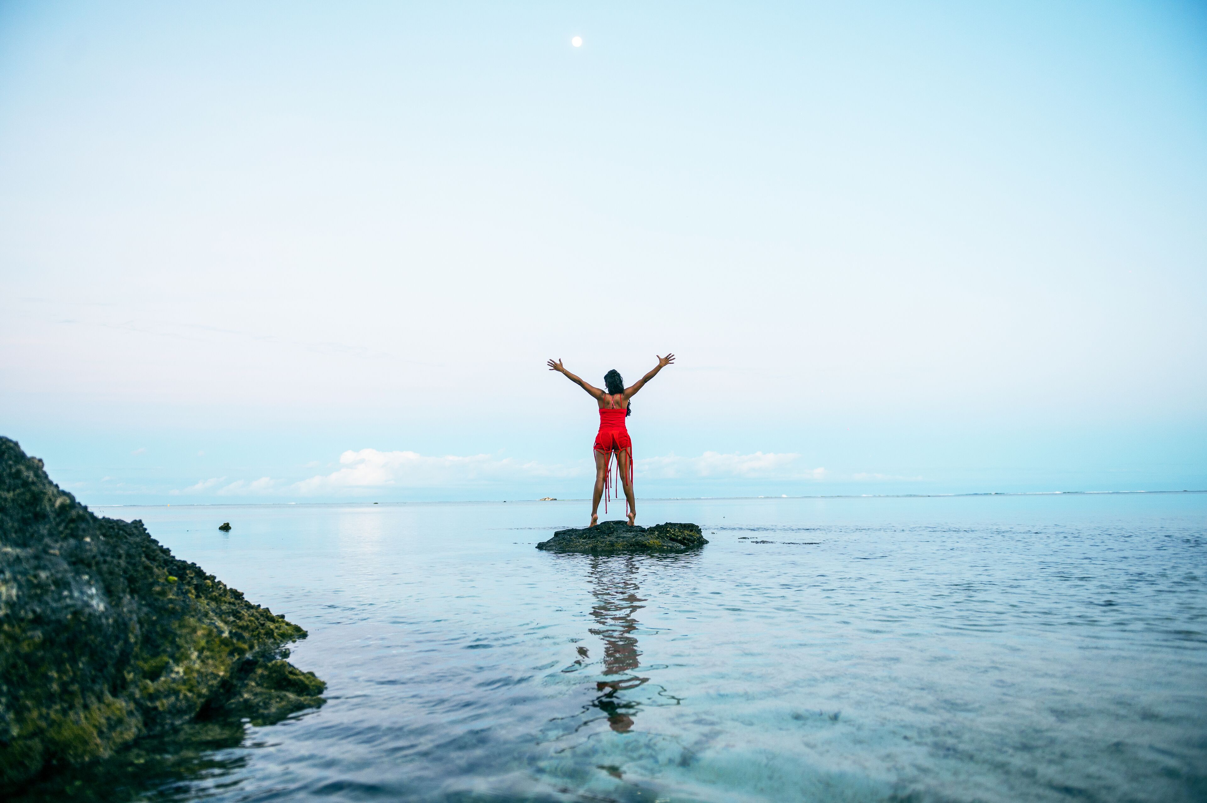 A person standing on a rock in the water with arms outstretched.