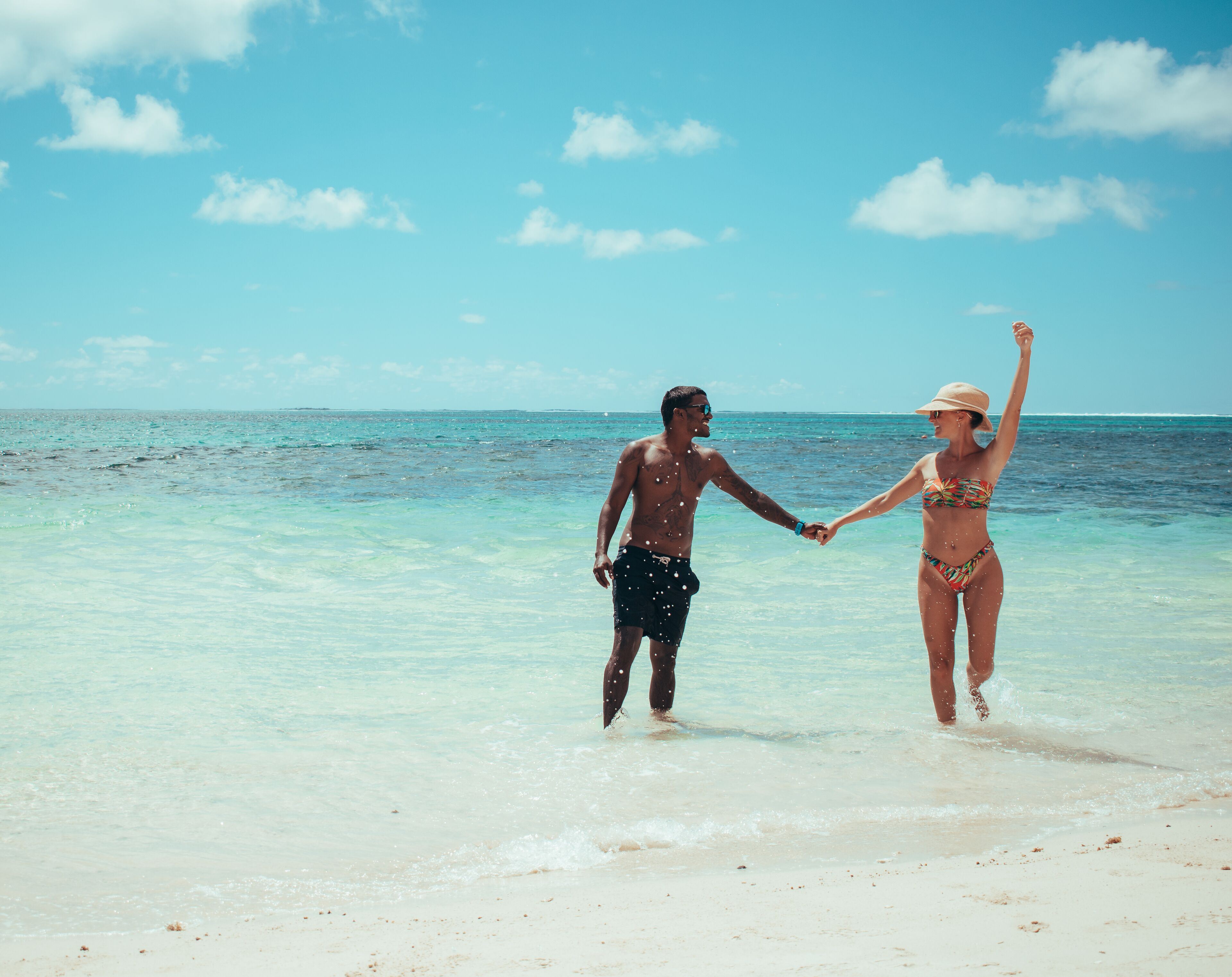 Two people holding hands on a beach with clear turquoise water and a clear sky.