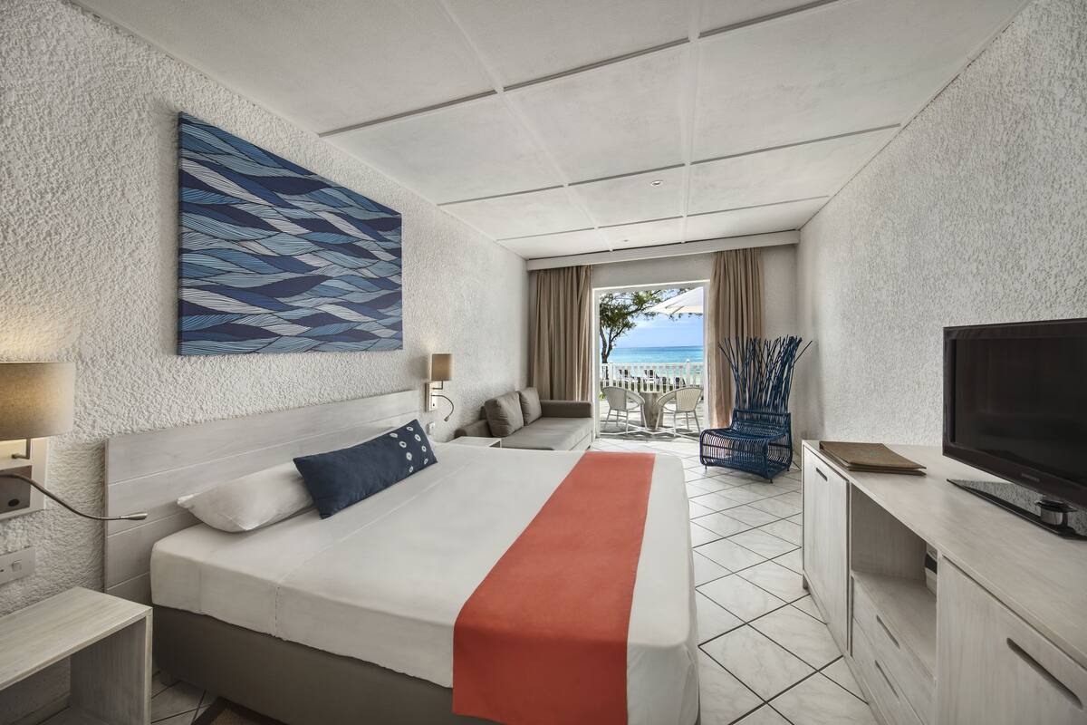 A hotel room with a bed, a TV, a desk, and a view of the ocean.