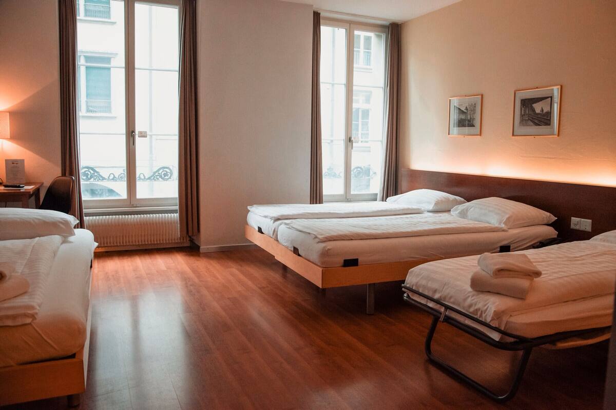 Habitació d'hotel amb dos llits, una taula de treball i una finestra amb cortines.