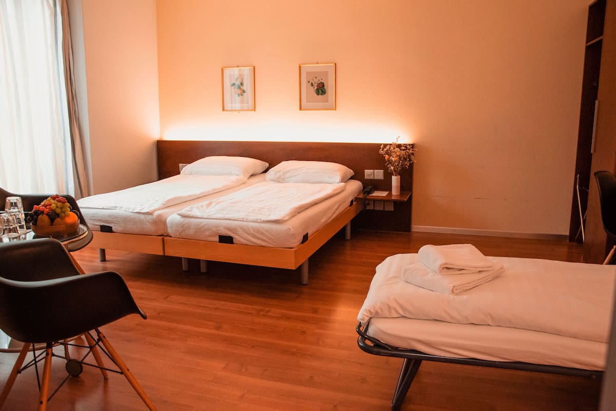 Habitació d'hotel amb dos llits individuals, un sòl de fusta, un escriptori amb una cadira i una taula petita amb un plat de fruita.