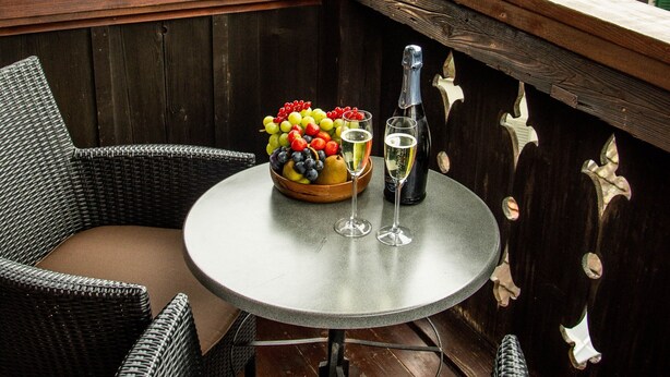 Ein Balkon mit Korbstühlen, einem runden Tisch und einer Obstschale mit Flasche und Gläsern.