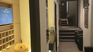 A hotel hallway with a reception desk, a blue sign, a staircase, and a wall-mounted shelf. - Royal Hotel (Brussels)