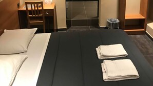 A hotel room with a large bed, a wooden desk, a chair, a wardrobe, and a small trash bin. - Royal Hotel (Brussels)