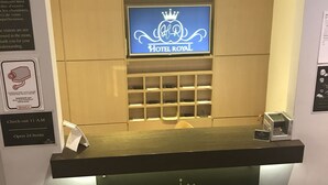 A reception desk with a digital screen displaying the Hotel Royal logo, a check-out sign, and a 24-hour check-out notice. - Royal Hotel (Brussels)