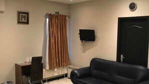 A room with two black beds, a black leather sofa, a desk with a chair, a television mounted on the wall, and a door with a handle. - Royal Hotel (Brussels)