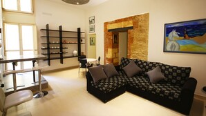 A modern living room with a black patterned sofa, a dining table with chairs, and a brick accent wall. - Khalisah (Palermo)
