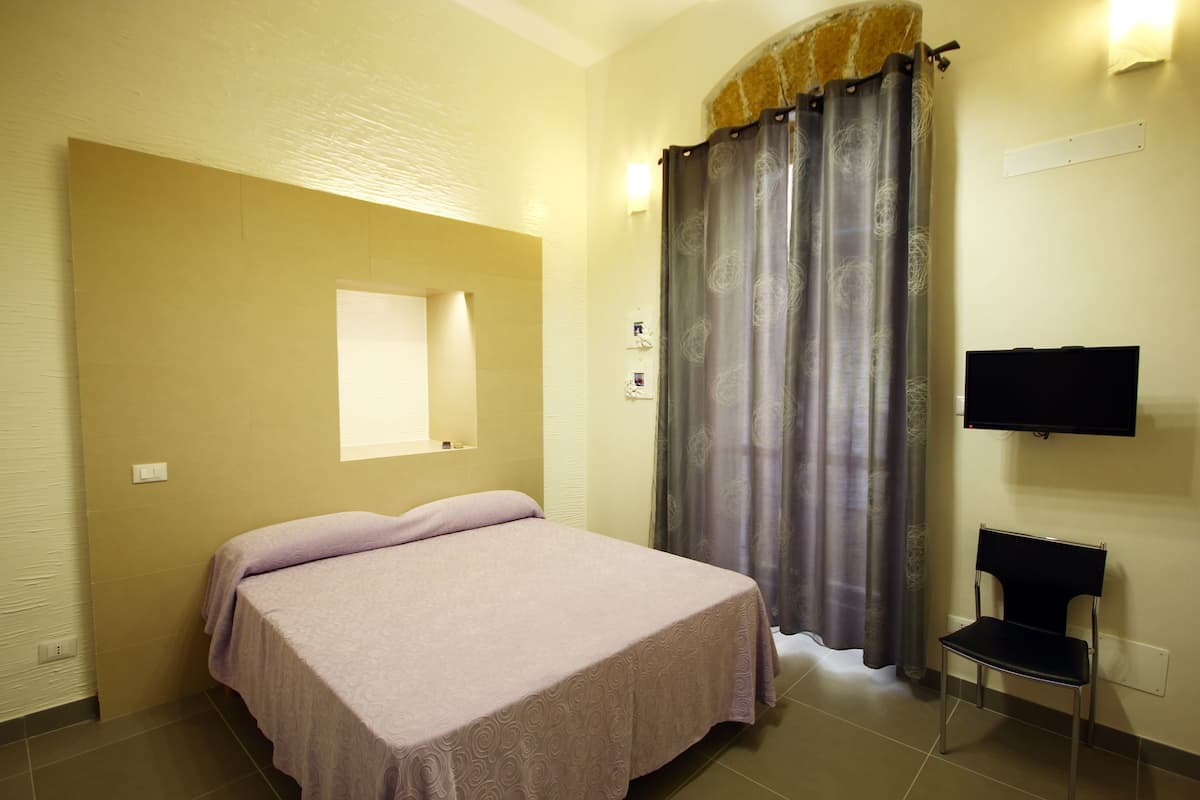 A bedroom with a bed, a chair, a television, and a window.